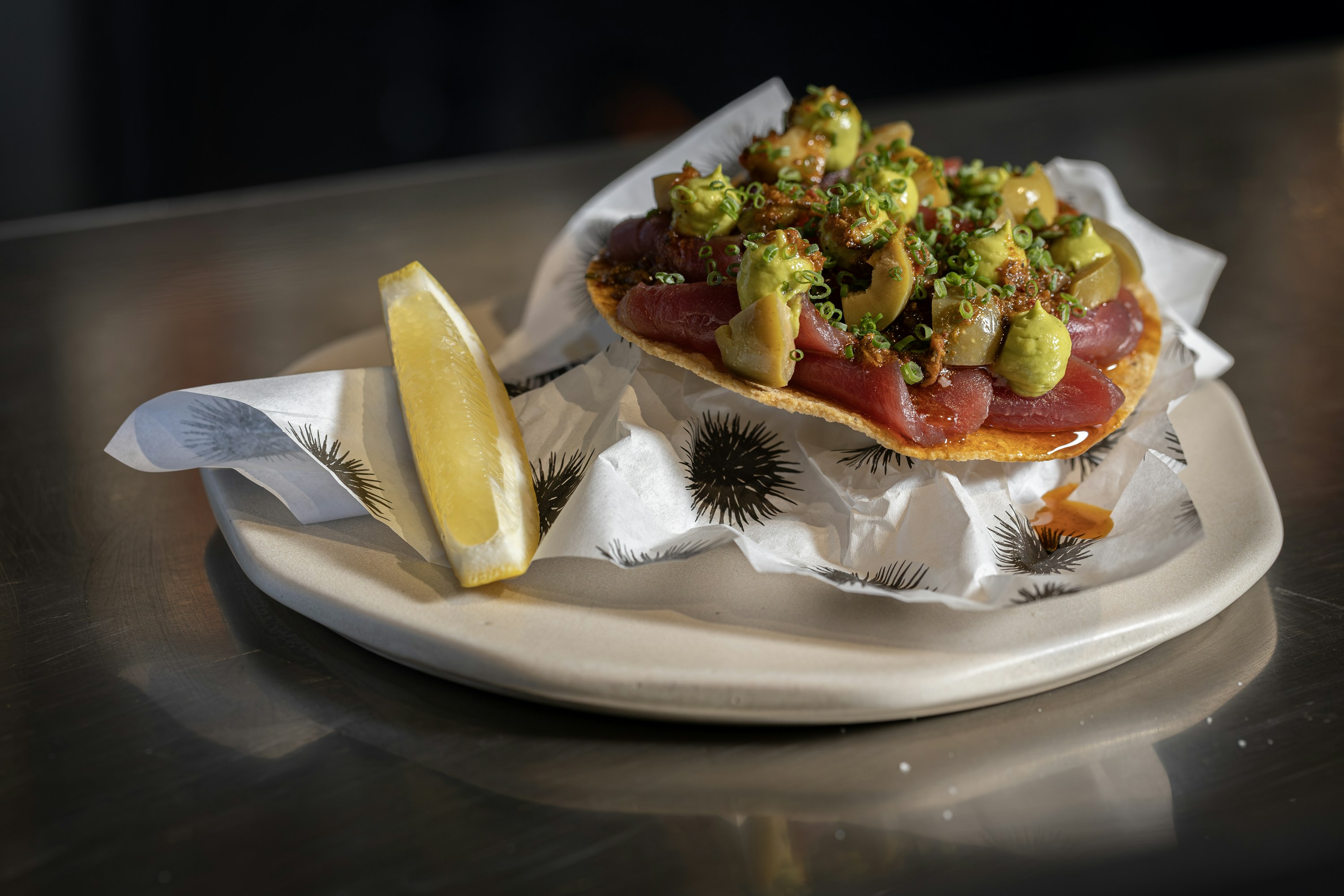 Tostada de atún con aguacate y una cuña de limón servida en un plato de restaurante