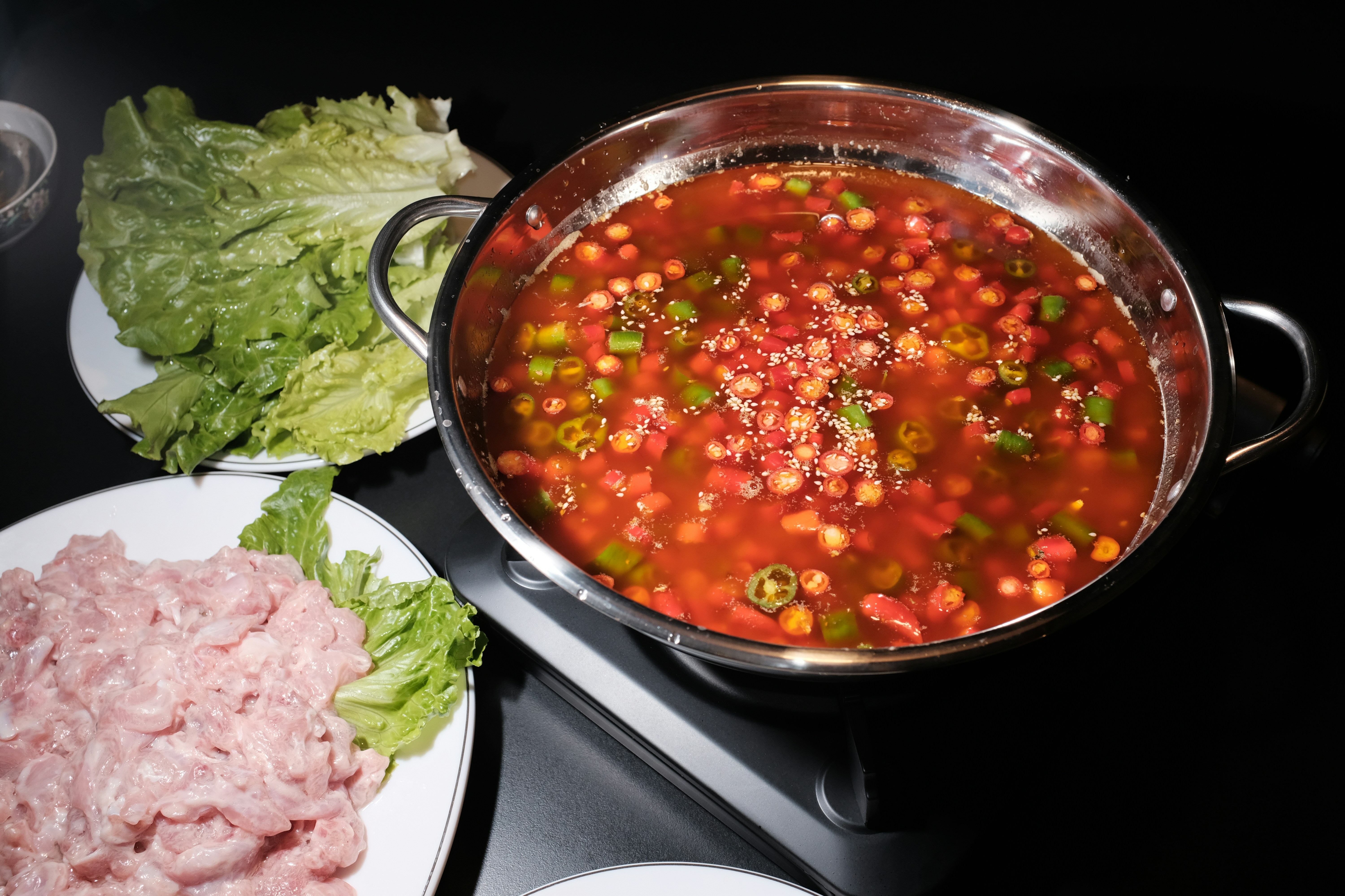 Olla de hot pot con caldo hirviendo junto a un plato de carne de cordero en láminas y lechuga