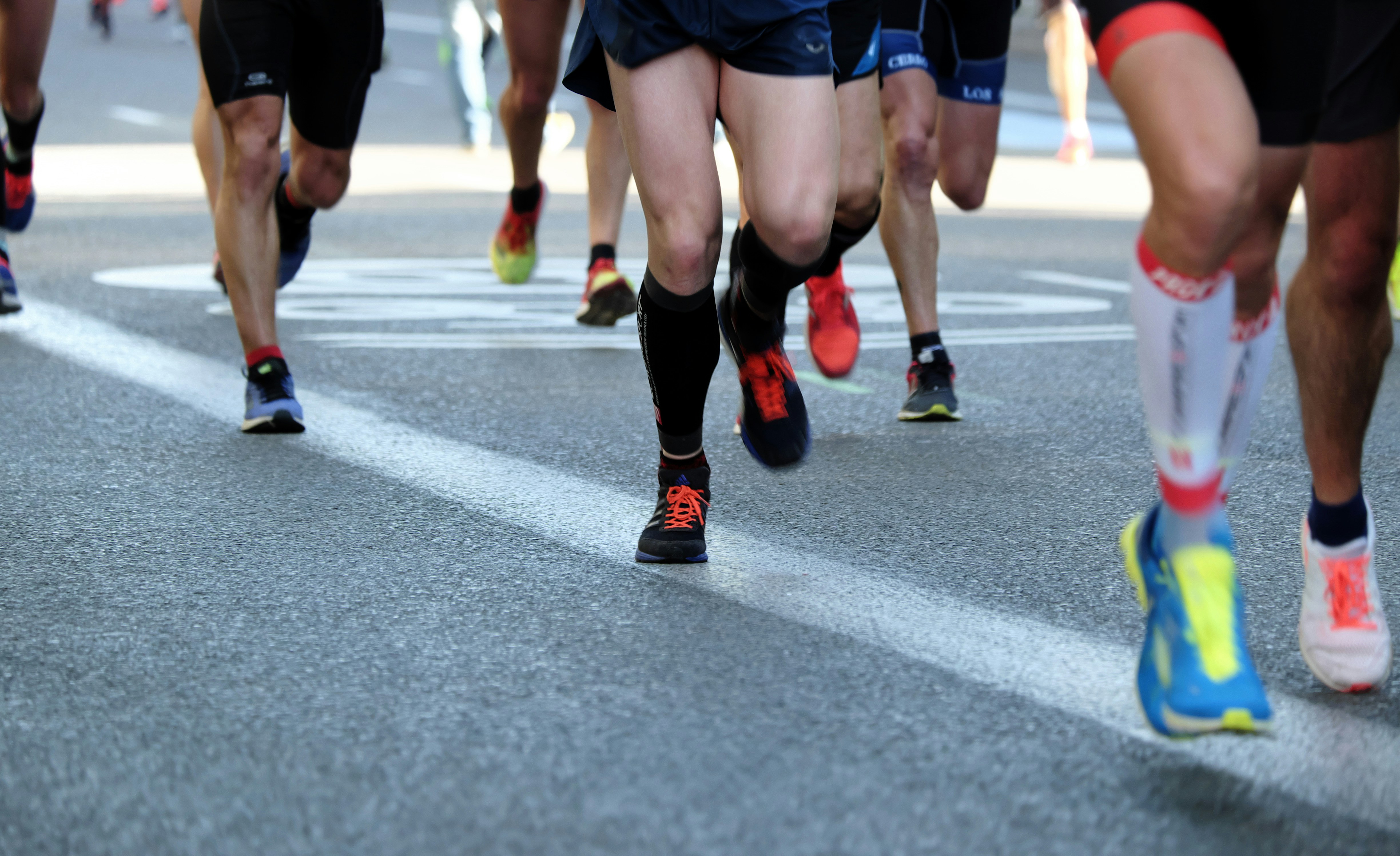 Piernas y tenis de corredores en plena zancada sobre el asfalto