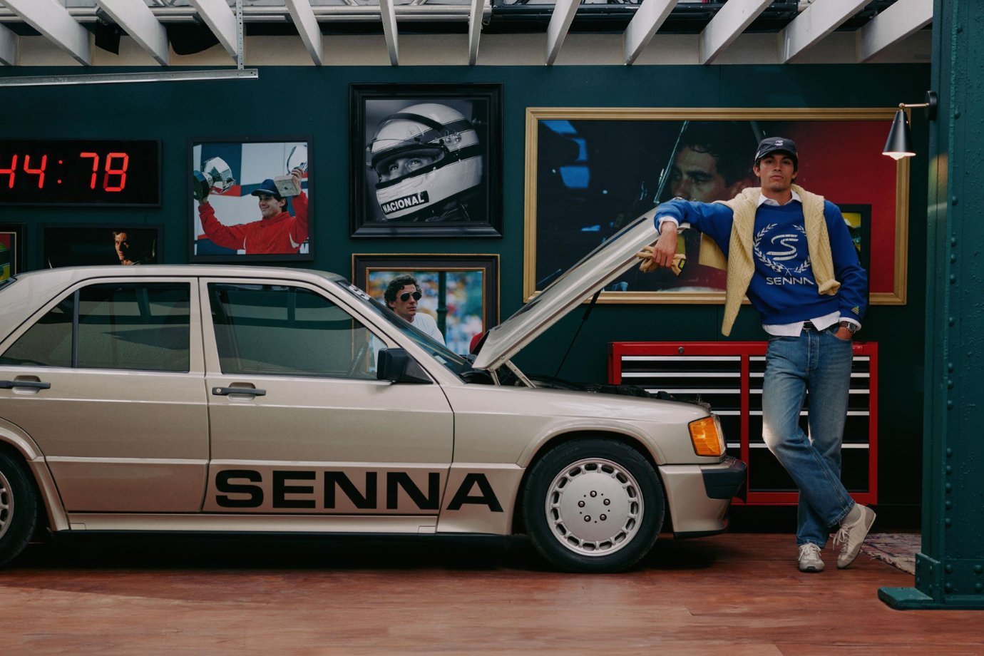 Modelo con suéter azul con el logo de Senna y un tejido amarillo sobre los hombros, junto a un sedán con el nombre del piloto